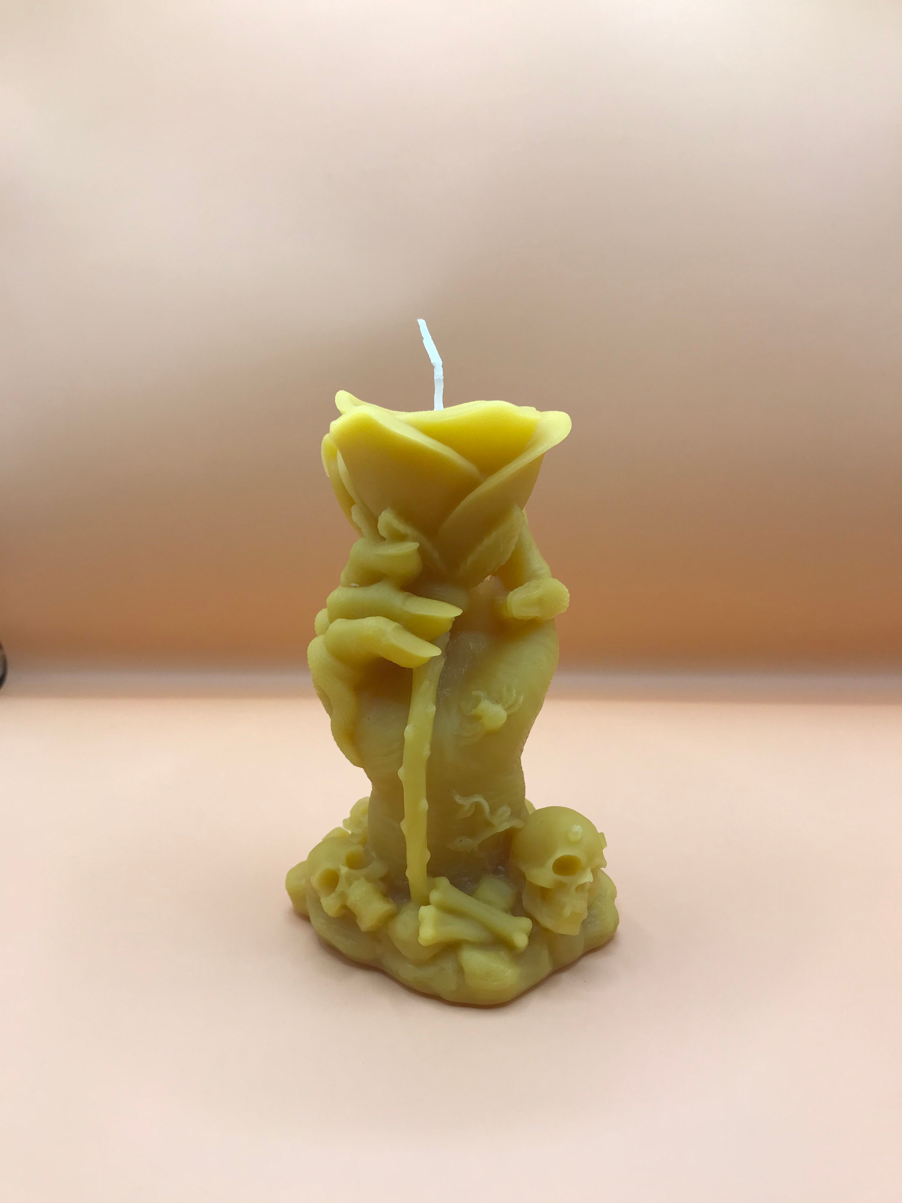 Hand-shaped candle holding a rose, skulls at base