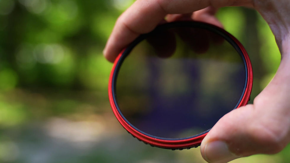 Hand holding a red-rimmed circular camera lens filter against a blurred green outdoor background.