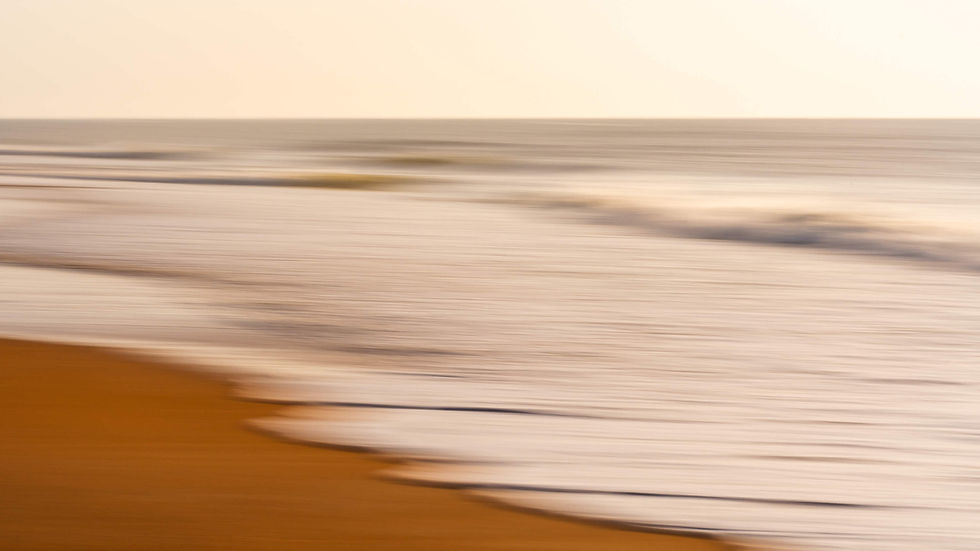 Blurred golden beach and ocean waves under a pale sky, creating a calm, motion-swept seascape.