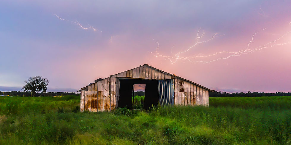 Abandoned barn in a grassy field under a pink storm sky, with lightning flashing overhead.