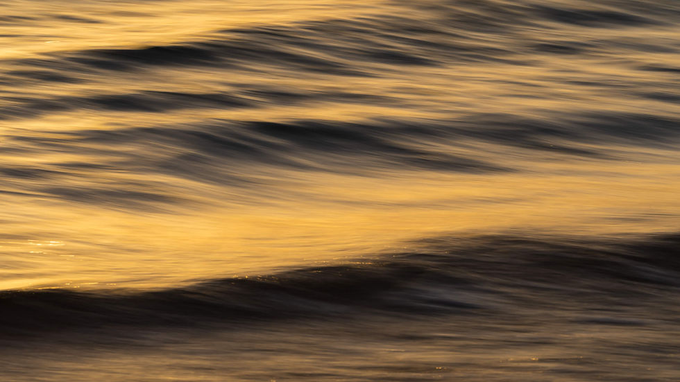 Golden sunset light shimmering across blurred ocean waves, creating a calm, abstract seascape with warm gold and dark gray tones.