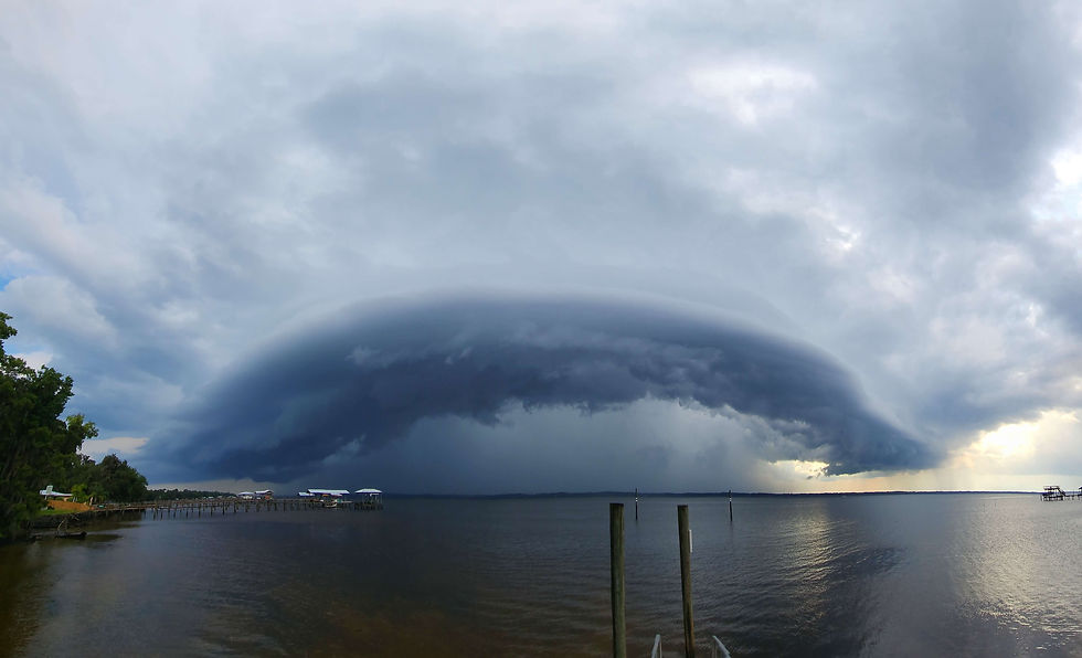 Massive dark storm cloud rolling over the St Johns River, with docks and trees along the shoreline under an ominous gray sky. Riverdale boat ramp.