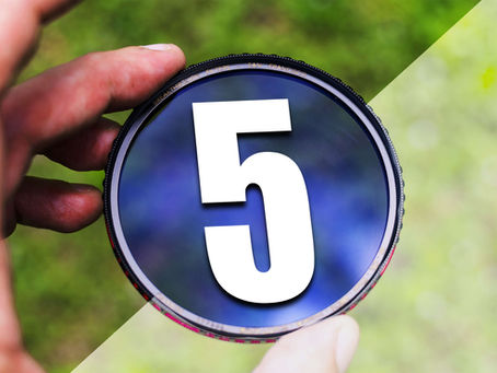 Hand holding a blue camera filter marked 5, with BREATHTHROUGH FILTERS SAN FRANCISCO on the rim, against a blurred green background.