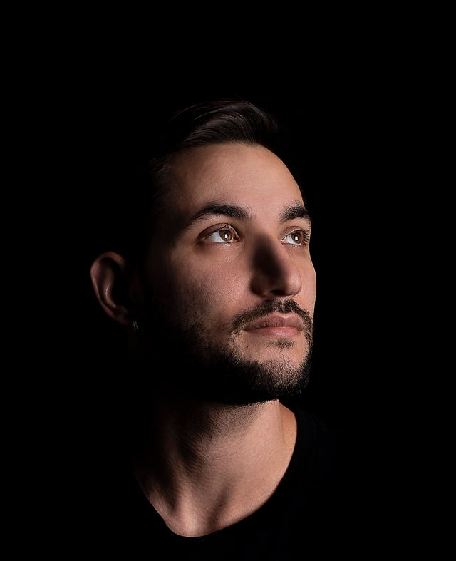 man with a beard looking up to the top right with light on his face in a black background