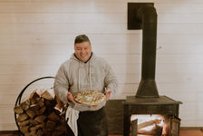 Chef holding pizza in front of a pizza oven, firewood, THE KAATSKELLER.