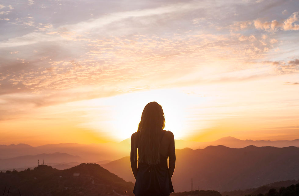Alt text: Decoding parts work, image of a woman with long hair stands and overlooks a mountain range while the sun rises.