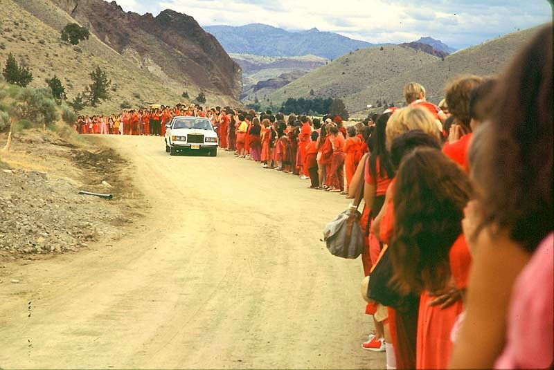 Rajneesh's followers line up in their freshly-dyed robes for the daily blessing as he's chauffeured by in his Rolls Royce. He would eventually own ninety-three of them.