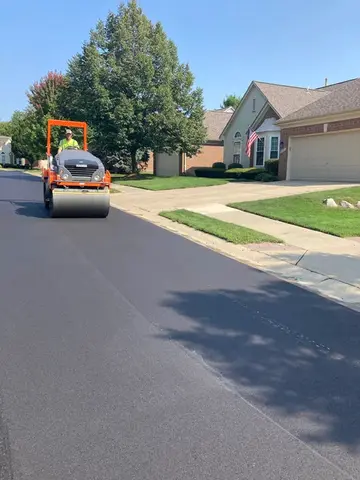Road roller compacting fresh asphalt paving on a residential street.