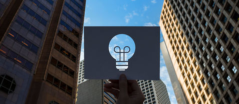 A card with a lightbulb cut being held up by a man in the middl of a city
