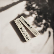 AI-generated product mockup of two boxes of lip gloss, shown on a beige surface with soft tree-shadow lighting