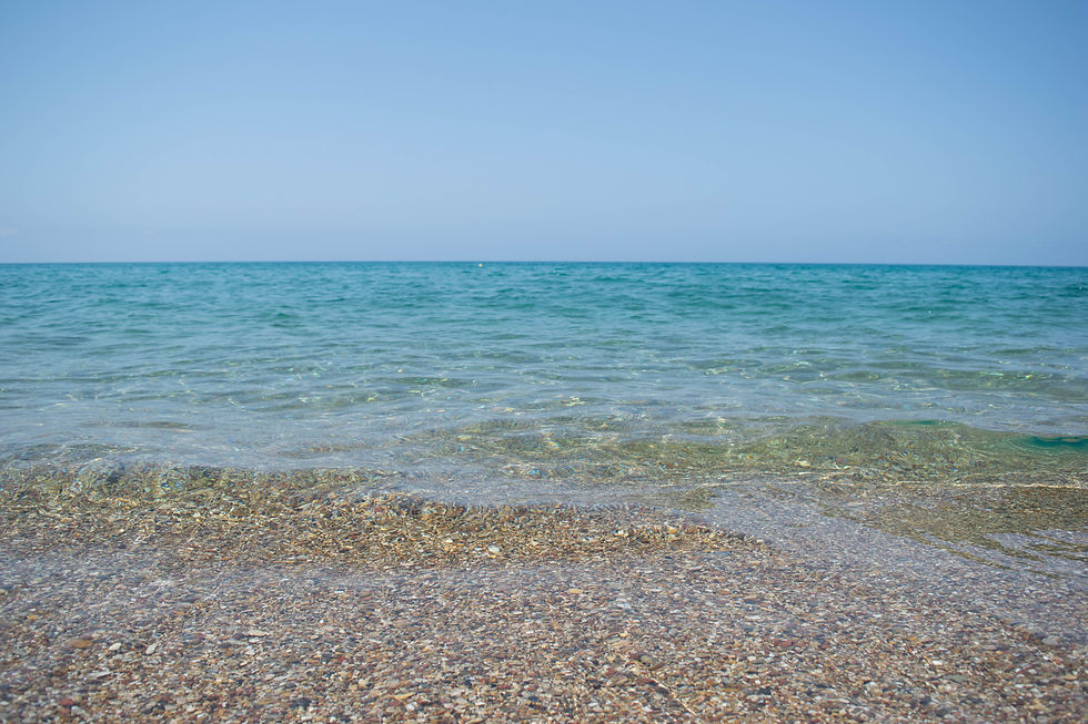 An image of just the sea and sky. The sea is perfectly clear, and you can see all the sand and pebbles. The sea is turquoise blue and calm, with small undulations. The upper third of the image is clear blue sky.