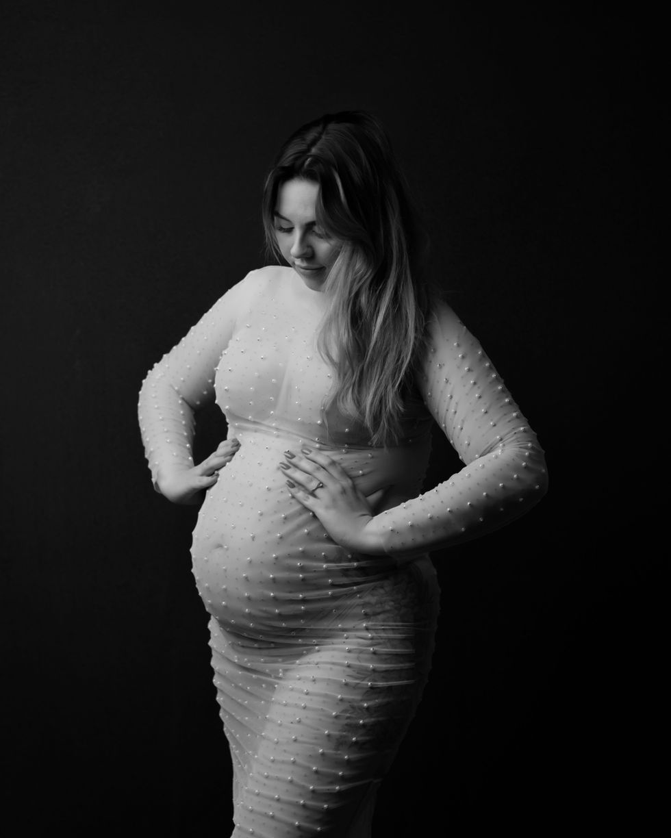 a pregnant woman in a pearl dress holds her belly