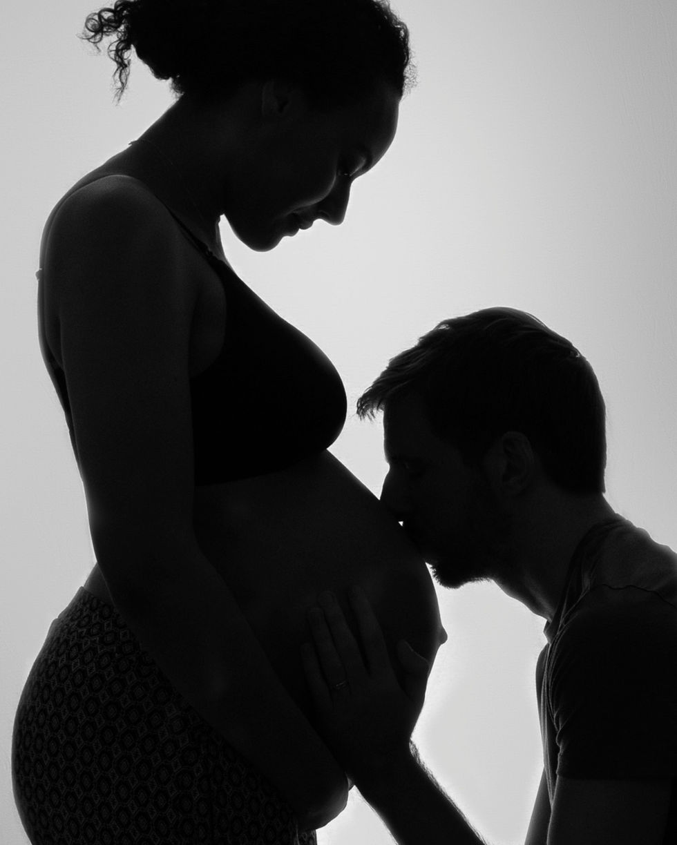 a man kisses a pregnant woman 's belly in a black and white photo
