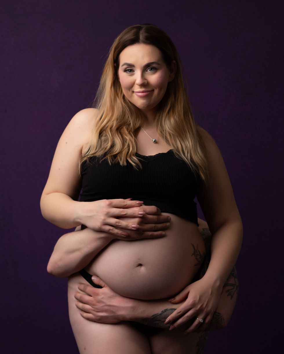 a pregnant woman in a black tank top is being held by a man