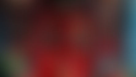 Red door with glass panels, flanked by blue walls. Elegant chandelier above. Two red chairs and a small table with a plant in front. Cozy vibe.