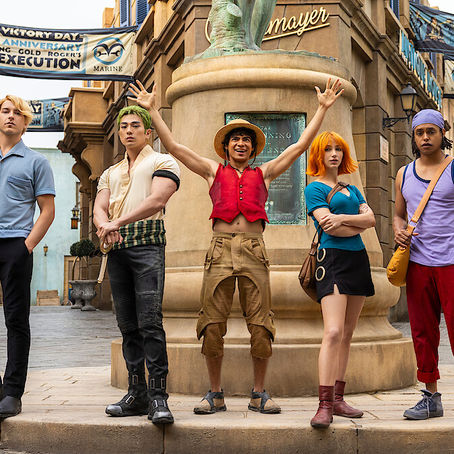 Five people stand in a lively street beneath banners. One person excitedly raises arms. Bright outfits contrast the stone background. Text: Marine Victory Day.