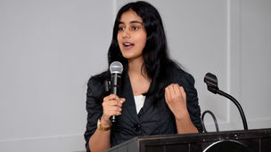 Hanna at a speaking engagement, wearing a black striped blazer. Via Hanna Grover.
