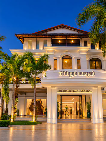 The Riverfront Central hotel facade at night with palms.