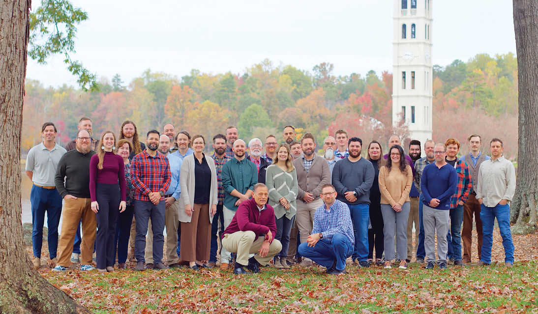 Daniel Builders team photo taken at Furman University by the lake with the bell tower in the background.