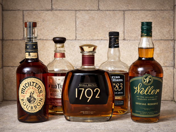 A selection of top bourbons available in Canada for under $100, featuring Michter's, Wild Turkey, 1792, Evan Williams, and Weller Special Reserve displayed against a brick backdrop.