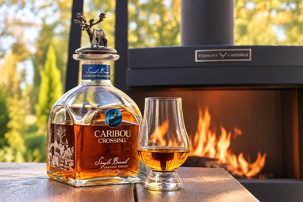 Caribou Crossing single barrel Canadian whisky bottle and glass on a table by an outdoor fireplace, warm sunset glow