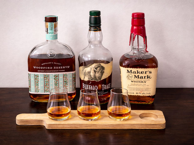 A tasting session featuring three iconic bourbons: Woodford Reserve, Buffalo Trace, and Maker’s Mark, elegantly showcased with three poured samples.