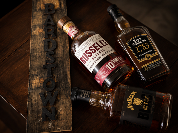 A selection of fine Kentucky bourbons, including Russell's Reserve, Evan Williams 1783, and Jim Beam, elegantly displayed on a wooden surface marked with "Bardstown," highlighting the heart of bourbon country.