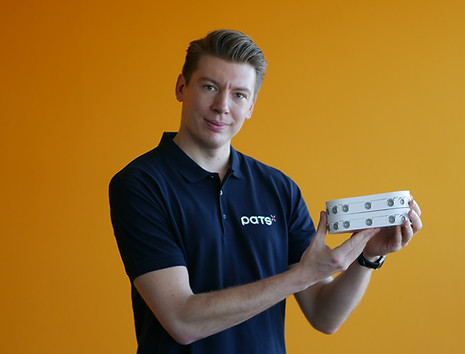 Man wearing a PATS shirt holding a PATS-C device against an orange background