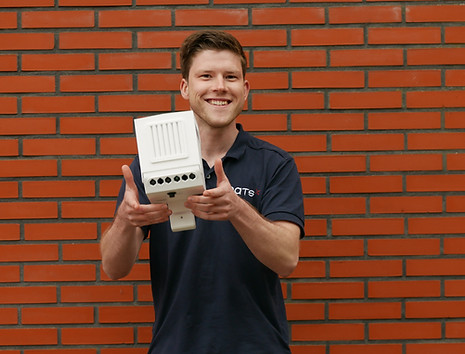 Man wearing a PATS shirt smiling and holding a PATS-C device in front of a brick wall