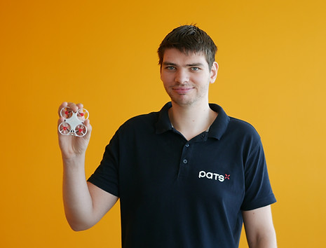 Man wearing a PATS shirt holding a small PATS drone against an orange background