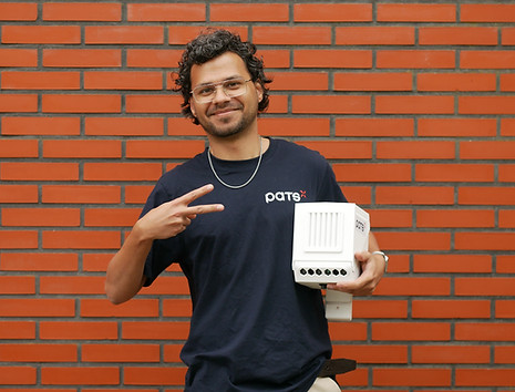 Man wearing a PATS shirt holding a PATS-C device and making a peace sign in front of a brick wall