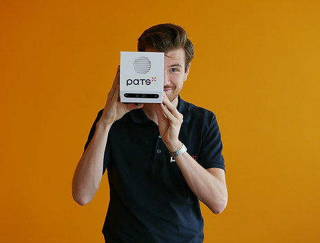 Man wearing a PATS shirt holding a PATS-C device against an orange background