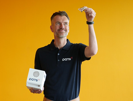 Man wearing a PATS shirt holding a PATS-C device and a small drone against an orange background