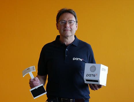 Man wearing a PATS shirt holding a Trap-Eye device and a PATS-C unit against an orange background