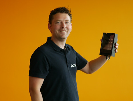 Man wearing a PATS shirt holding a PATS-C installation lamp against an orange background