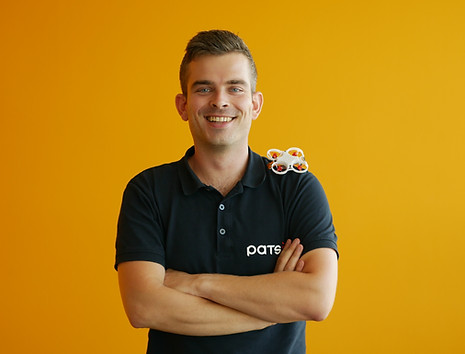 Man standing with folded arms wearing a PATS shirt with a small drone on his shoulderG