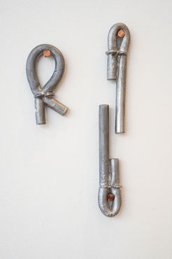 Three sculptures hanging on a white wall with copper hardware. Two of the sculptures mirror each other and the third is hung off to the side.