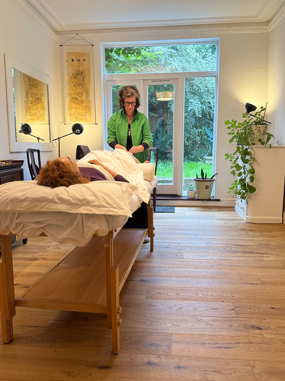 Abigail treating a patient in the Acquaviva clinic. A person lying on a treatment couch and Abigail stands at her feet preparing, the walls are white and there are large French doors overlooking a leafy garden.