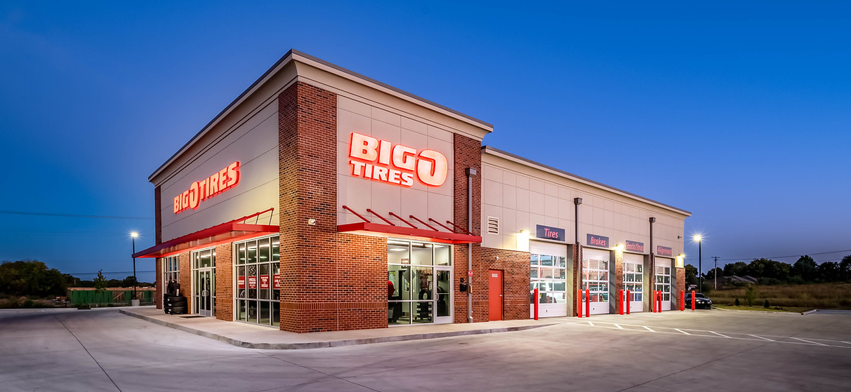 Exterior photo of Big O Tires showing a dark blue sky, empty parking lot and the brick and white plaster walled building.