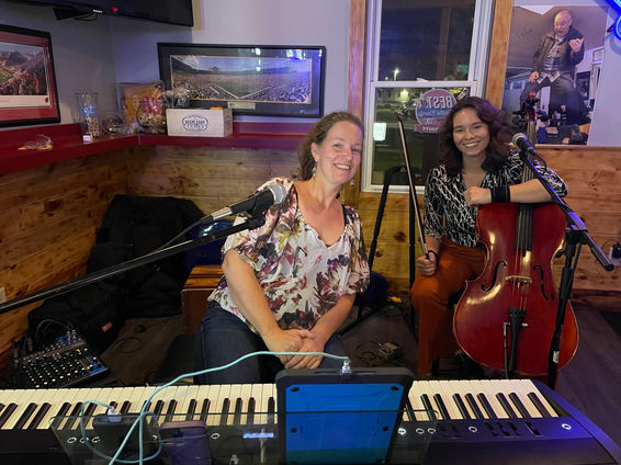 Bird & Bloom members, Rebecca and Maddie, sitting with instruments at Spanky's Sports Bar and Grill.