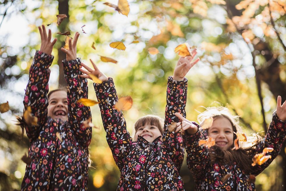 Three girls smiling and throwing leaves in the air at their fall family photoshoot in Essex by Zee Gunchev.