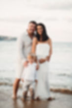 A family of three standing on a beach at sunset, dressed in light-colored clothing. Taking maternity portraits with Zee Gunchev an Essex maternity photographer.
