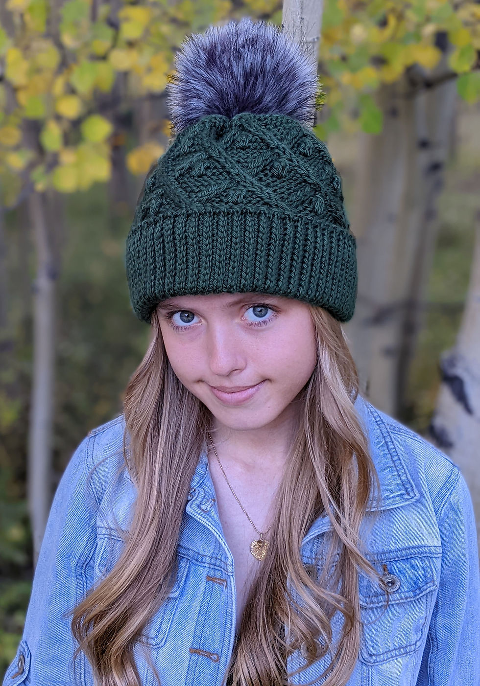 Thumbnail: Deep green tunisian crochet winter hat with wide ribbing. Syled with cables, bobbles and large fur pom pom