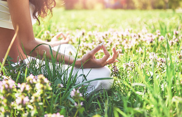 Tan skinned woman sitting in sunny grass with flowers meditating