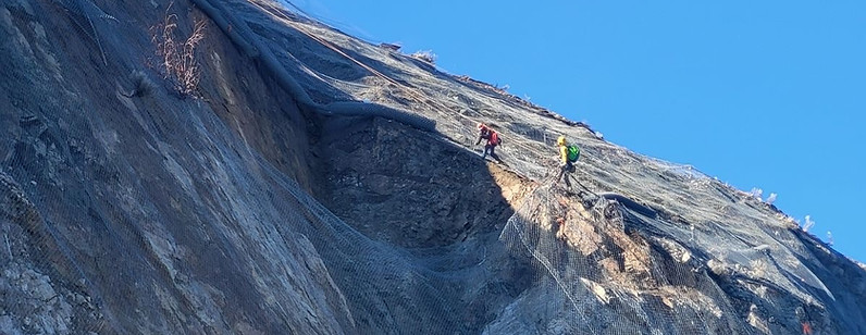 Dynamite Construction crew performing high-angle rope access rock scaling on vertical rock face, BC