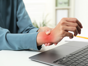 Person touching their painful wrist in front of a laptop