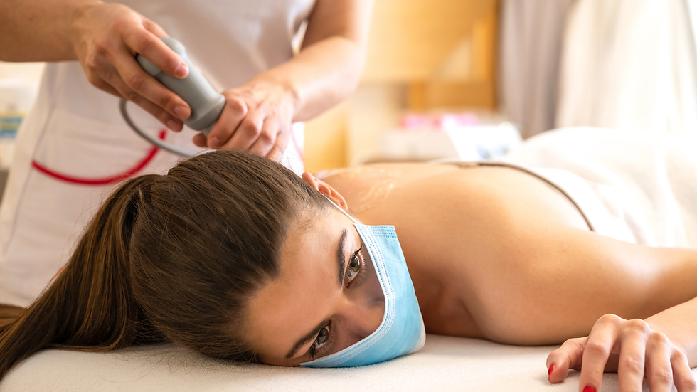 A young woman receives SoftWave therapy for shoulder pain, lying comfortably in a clinic while a healthcare professional applies a handheld treatment device.