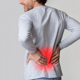 Close-up of a man seen from behind, holding his lower back with both hands, showing signs of pain and discomfort.