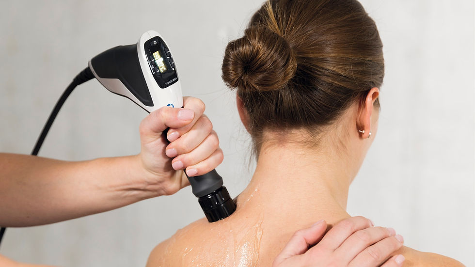 A healthcare professional using a portable shockwave therapy applicator with a digital display on a woman's upper back and neck area, applying gel for the procedure in a medical environment.