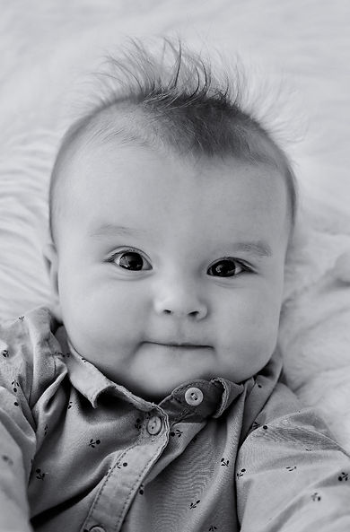 Schwarzweiß-Portrait eines Babys mit zerzausten Haaren und einem ganz leisen Schmunzeln